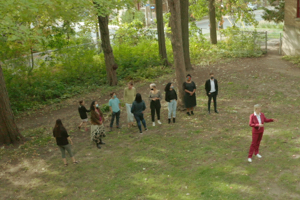 An aerial view of Saint Paul University students, discussing in a forest on campus, with Chantal Beauvais, rector of Saint Paul University, standing ahead of the group