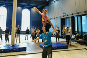 A group of performers in one of The 7 Fingers' training studios, with a man climbing onto another man's shoulders in the foreground